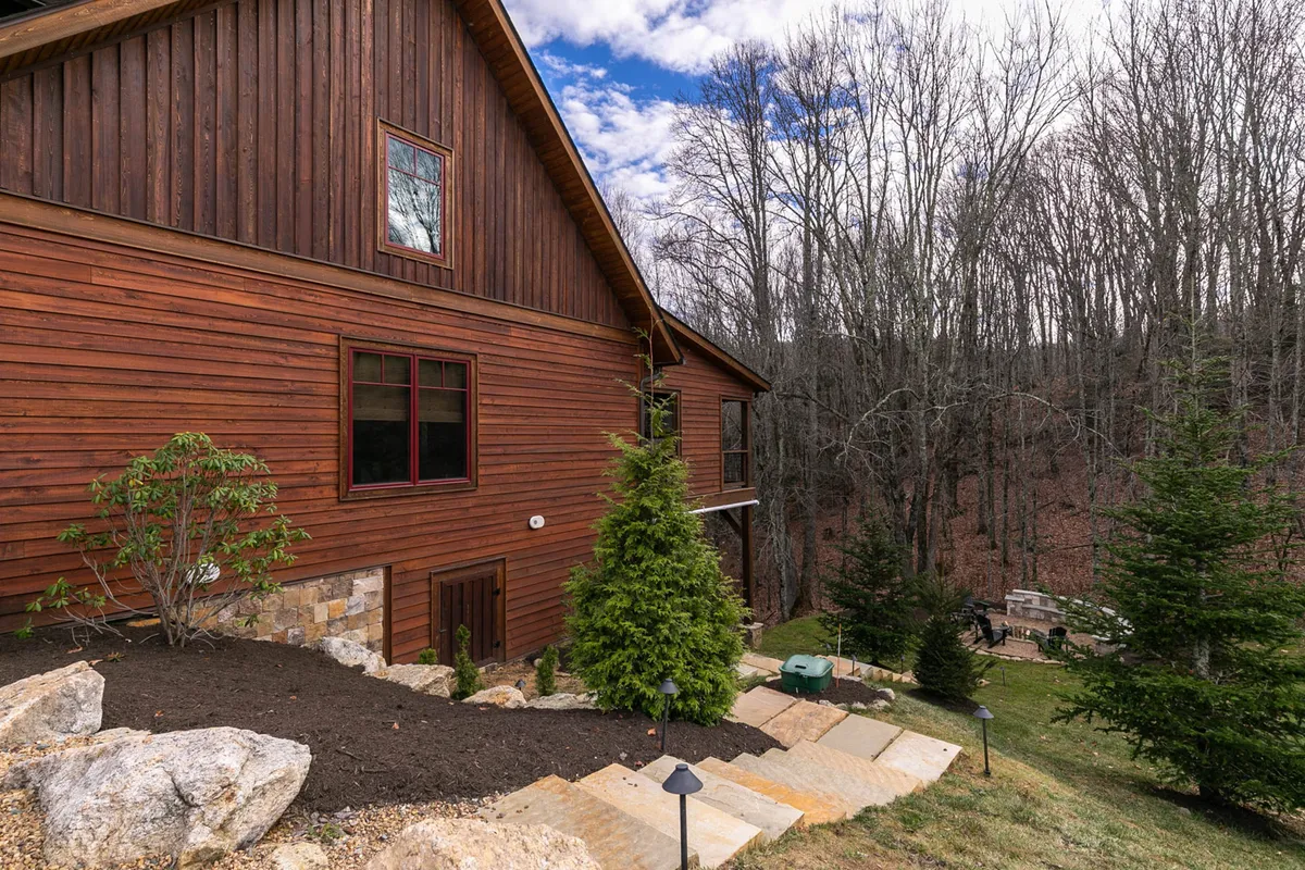 This exterior image showcases the wooden façade of the home with a landscaped garden and steps leading up to the entrance. The greenery and natural setting are prominent, suggesting easy access to nature and trails nearby.