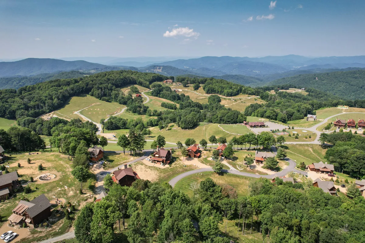 This image presents a sweeping view of rolling hills adorned with scattered cabins and winding roads, all surrounded by dense greenery. The scene evokes a strong sense of the outdoors and hints at the extensive trail system and natural beauty accessible from the property.
