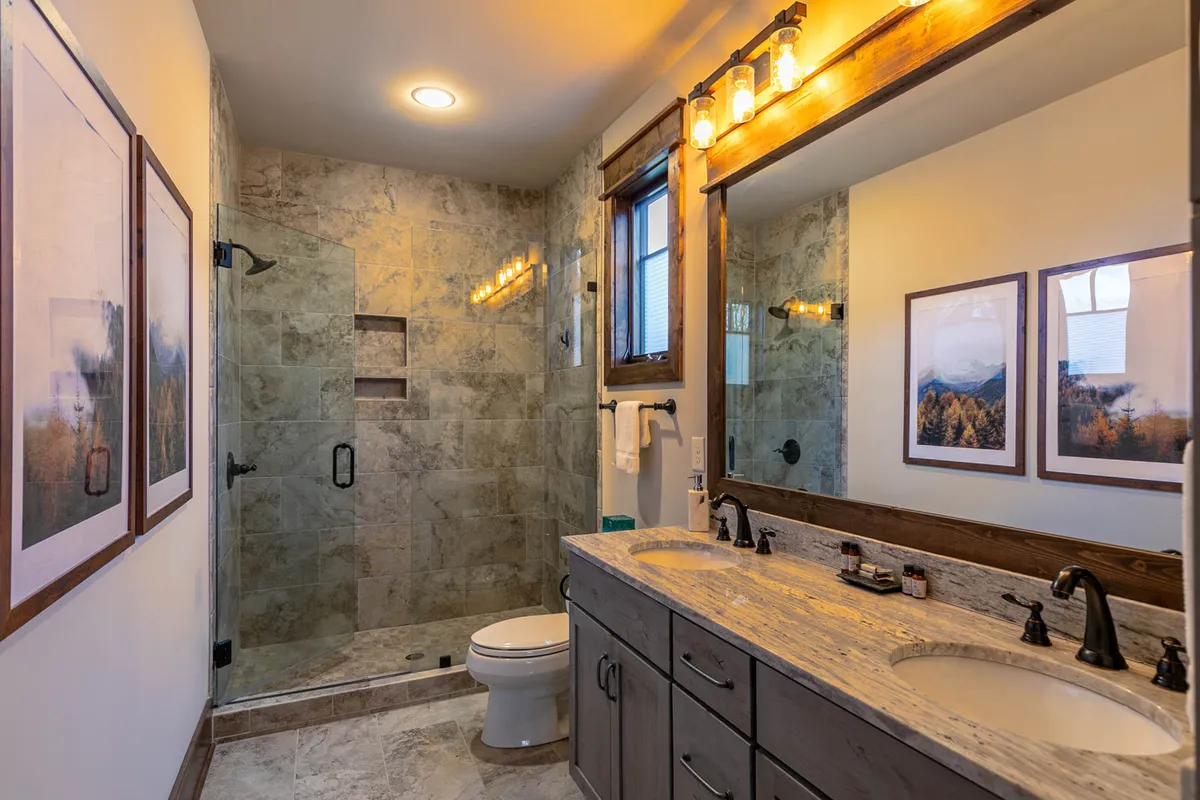 A modern, spa-inspired ensuite bathroom with a spacious walk-in shower, double granite vanities, and elegant framed artwork. The bathroom is bright and inviting, with ample space for relaxation and self-care routines.