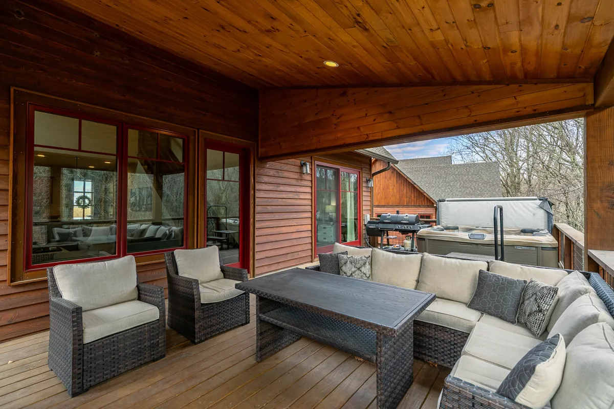 A welcoming wooden deck with comfortable seating and a hot tub, set amidst a forested landscape. The scene captures a space designed for both relaxation and socializing outdoors, with room for groups to gather and enjoy the fresh mountain air.