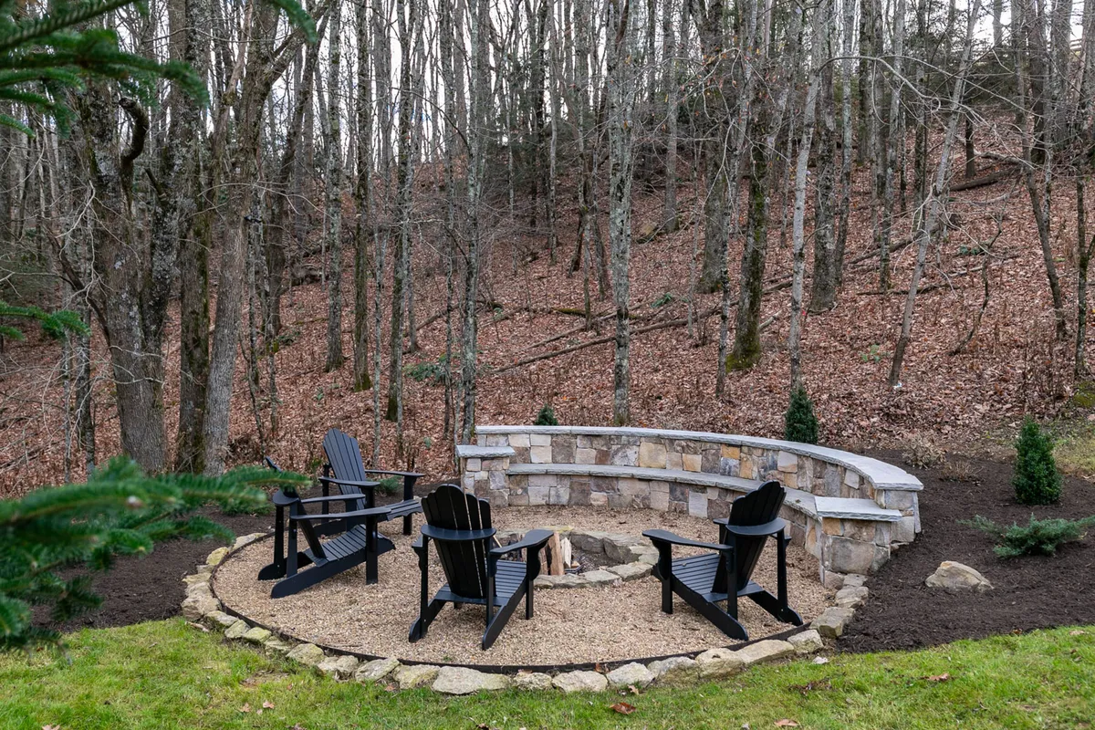 A stone seating area surrounds a cozy fire pit nestled among mature trees, ideal for evening gatherings. The setting is tranquil and inviting, perfect for storytelling, stargazing, or enjoying the crisp mountain air.