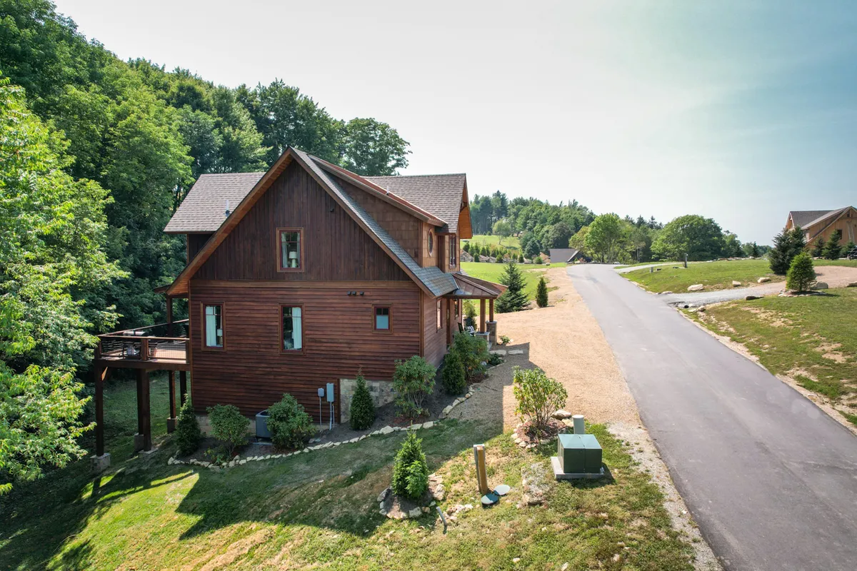 The image features a charming wooden home embraced by lush green trees with a meandering pathway leading up to it. The sense of seclusion and natural beauty highlights the surrounding mountain environment.