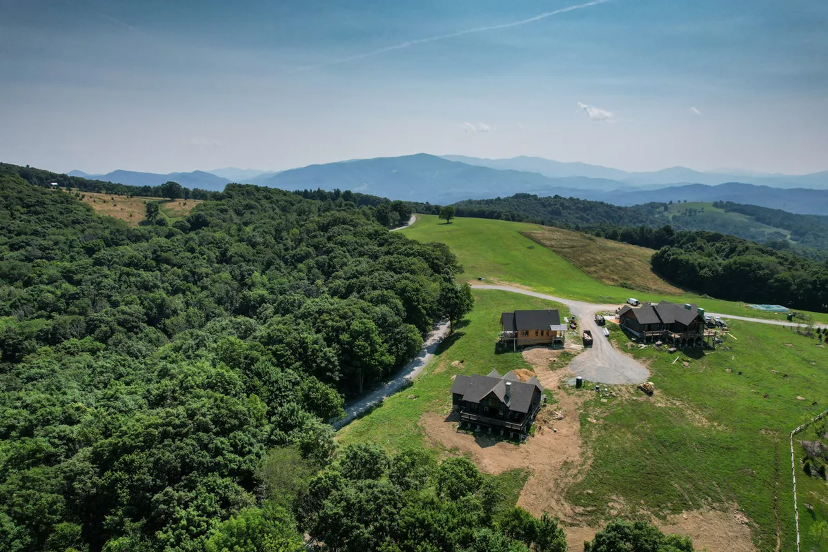 A sweeping view of green fields stretches toward distant mountains, dotted with houses and framed by open skies. The landscape conveys tranquility and the appeal of outdoor exploration with scenic backdrops.