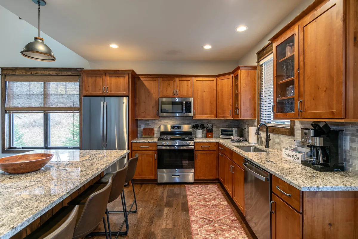 A close-up of a modern kitchen with a granite island, stainless steel appliances, and elegant wood cabinetry. The island offers ample seating, and the setup is perfect for interactive meal preparation or casual dining.