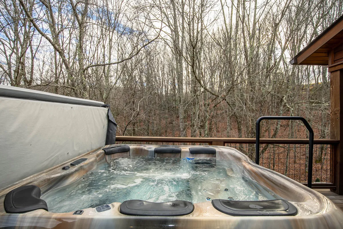 This image features a hot tub set on a wooden deck, surrounded by lush trees and a sturdy deck railing. The view hints at a tranquil forest setting, ideal for relaxing in privacy while soaking in the natural beauty around the home.