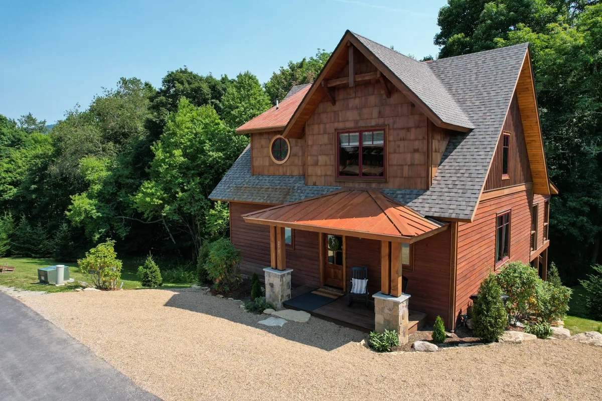 The image showcases the beautiful wooden exterior of Overlook Nook at Eagles Nest, nestled among landscaped gardens. A spacious porch with inviting chairs hints at cozy mornings with coffee or relaxing evenings under the stars, all set against the picturesque backdrop of Banner Elk's mountains.