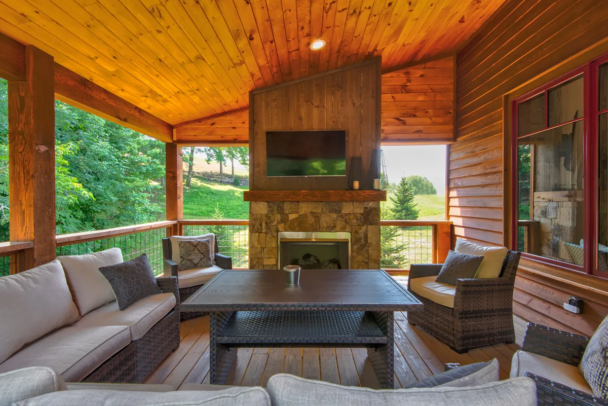 An exterior patio designed for comfort, featuring a stone fireplace, cozy seating, and a wood-paneled ceiling. The setup is ideal for outdoor gatherings, sunset watching, and socializing by the warmth of the fire.