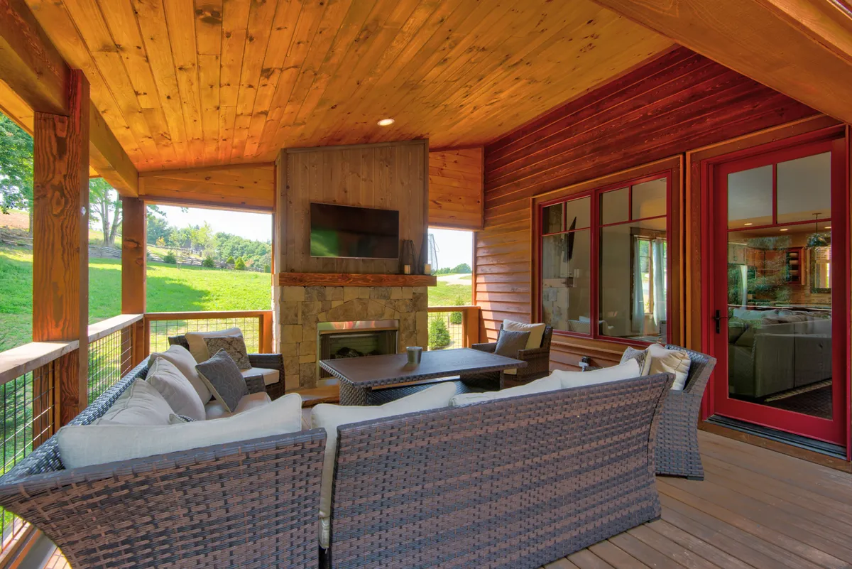 An inviting patio showcases a woven seating arrangement, a stone fireplace, expansive windows looking into the home, and a warm wooden ceiling. The scene is set for both intimate mornings with coffee and lively gatherings with friends, all with mountain vistas in easy reach.