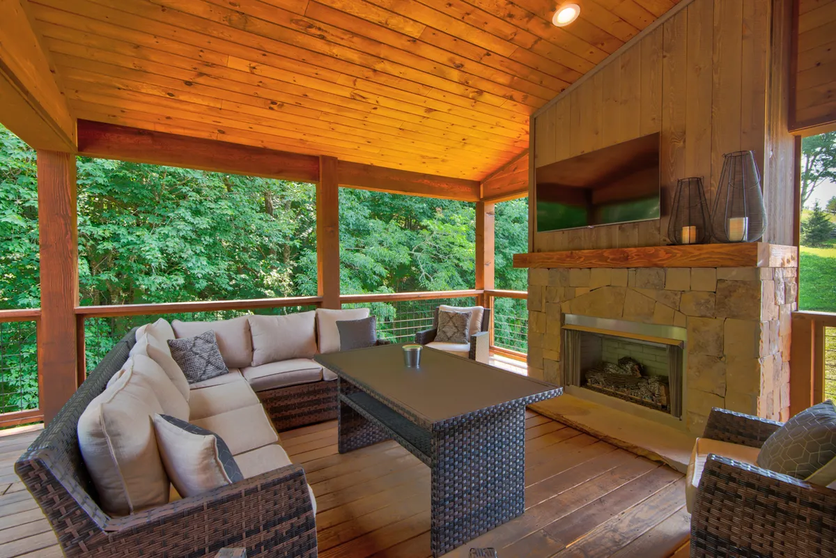 This image features a luxurious outdoor seating area with comfortable chairs, a striking stone fireplace, and a wooden ceiling overhead. The space is surrounded by nature, creating a perfect setting for relaxation and outdoor entertaining. The atmosphere exudes comfort and tranquility, with an inviting ambiance for enjoying sunsets or stargazing.
